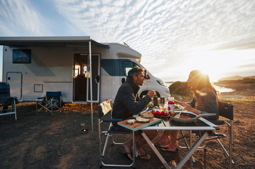 Romantisches Nachtessen während dem Camping-Urlaub vor dem gemieteten Wohnmobil bei perfekter Sonnenuntergangsstimmung am Meer.